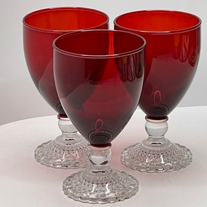 May include: Three red glass goblets with clear, textured bases. The goblets are round and have a wide, open top.