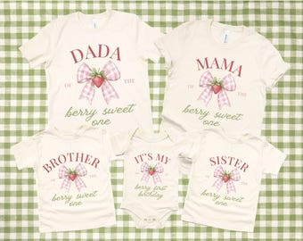 May include: Set of five cream-coloured t-shirts with strawberry and bow designs. The shirts say "Dada of the berry sweet one", "Mama of the berry sweet one", "Brother of the berry sweet one", "Sister of the berry sweet one", and "It's my berry first birthday".