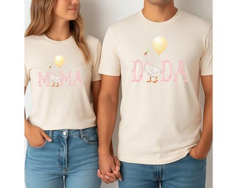 May include: A matching set of two cream coloured t-shirts with a goose graphic and the words "MOMA" and "DADA" in pink lettering.