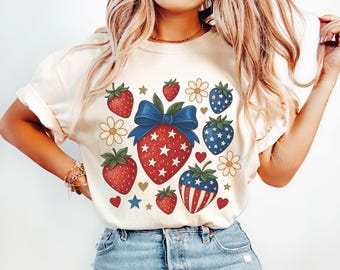 May include: A white t-shirt featuring a red, white and blue strawberry design. The strawberries are decorated with stars and stripes.