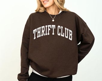 May include: A brown sweatshirt with the text "THRIFT CLUB" in white letters.