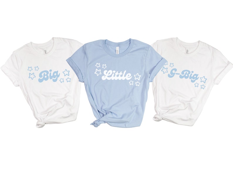 May include: Three white t-shirts with blue text and white stars. The shirts say "Big", "Little", and "G-Big".