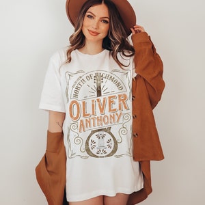 Op de afbeelding: Wit T-shirt met een vintage-stijl grafisch ontwerp met een banjo, de tekst "NORTH OF RICHMOND" en de naam "OLIVER ANTHONY".