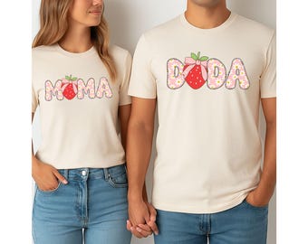 May include: A pair of cream-coloured t-shirts with a strawberry graphic. The shirt on the left says "MOMA" and the shirt on the right says "DADA".