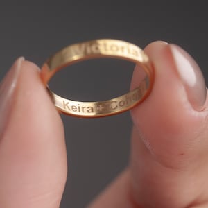 May include: A gold band ring with the inscription "Keira + Cohen" and "Victoria" on the outside of the band.
