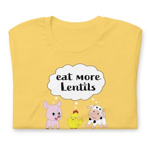 Puede incluir: Camiseta amarilla con una burbuja de pensamiento blanca que dice "eat more lentils". Un cerdo rosa, un pollo amarillo y una vaca blanca y negra miran hacia arriba a la burbuja de pensamiento.
