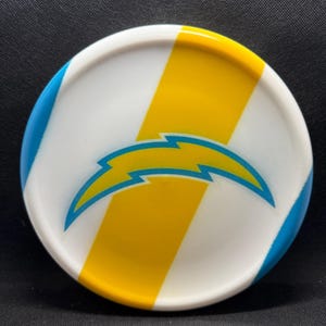 May include: A white disc with blue and yellow stripes and a blue and yellow lightning bolt logo. The disc is a sports item, likely for a game like disc golf or frisbee.