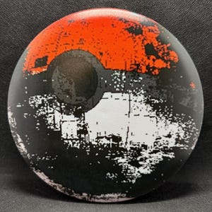May include: A round, black, white, and red disc with a pixelated design. The design resembles a Pokeball, a popular item from the Pokemon franchise.