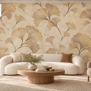 Könnte beinhalten: Ein Wandbild mit einem sich wiederholenden Muster aus hellbraunen und beigen Ginkgo-Biloba-Blättern auf einem strukturierten cremefarbenen Hintergrund. Das Design umfasst ein weißes, geschwungenes Sofa, einen runden Holztisch und einen beigen Sessel.