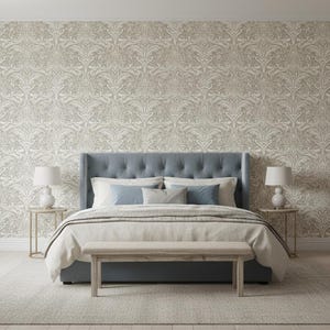 Puede incluir: Una cama con cabecero capitoné azul frente a un papel pintado con motivos en beige y blanco. La cama incluye un edredón claro, dos cojines azules y uno gris. Dos lámparas blancas se sitúan sobre pequeñas mesas auxiliares redondas.