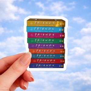 Puede incluir: Una pegatina con una pila de cajas de DVD de la serie de televisión Friends. Cada caja es de un color diferente y muestra el número de la temporada. La pila incluye las temporadas de la uno a la nueve, con el logotipo y el título de la temporada.