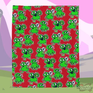 May include: A red blanket featuring a repeating pattern of green cartoon characters with the number "2" and peace signs. The characters have large eyes and are in various poses. The blanket has a soft, inviting appearance.