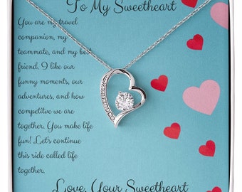May include: A silver necklace with a heart pendant and a clear crystal in the centre. The necklace comes in a blue box with a message that reads "To My Sweetheart" and "Love, Your Sweetheart".