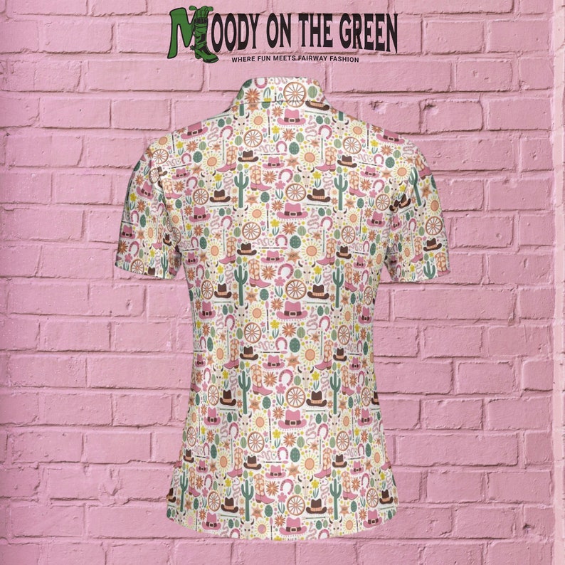 May include: A white short-sleeved button-down shirt with a colorful pattern of cowboy boots, hats, cacti, horseshoes, and wagon wheels. The text "MOODY ON THE GREEN" is printed on the back of the shirt.