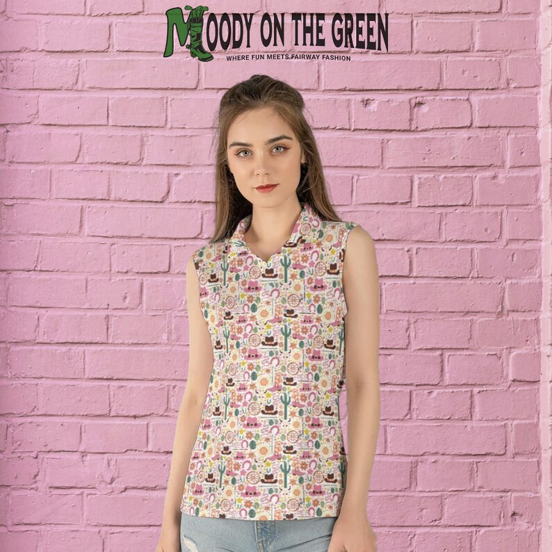 May include: A white sleeveless collared shirt with a colorful pattern of cacti, horseshoes, cowboy hats, and boots. The shirt has a v-neck and is made of a soft, comfortable fabric. The text "MOODY ON THE GREEN" is displayed at the top of the image.