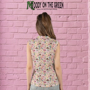 May include: A sleeveless white shirt with a colorful pattern of western-themed icons, including cacti, horseshoes, cowboy hats, and boots. The text "MOODY ON THE GREEN" is visible at the top of the shirt.  "WHERE FUN MEETS FAIRWAY FASHION" is also visible on the shirt.