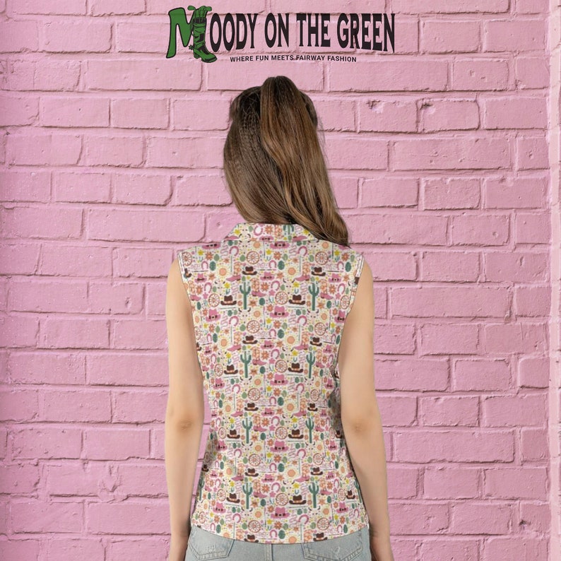 May include: A sleeveless white shirt with a colorful pattern of western-themed icons, including cacti, horseshoes, cowboy hats, and boots. The text "MOODY ON THE GREEN" is visible at the top of the shirt.  "WHERE FUN MEETS FAIRWAY FASHION" is also visible on the shirt.