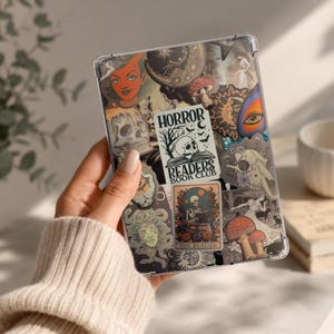 May include: A clear tablet case covered in various stickers featuring occult and dark themes, including a central white rectangular sticker with the text "HORROR READERS BOOK CLUB" above a skull, a skeleton reading a book, mushrooms, and eyes.