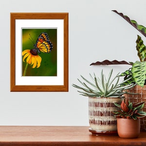 Gouache painting titled 'Flutterby' features a yellow monarch butterfly on a cone flower against a green background. Adds natural elegance to any space.