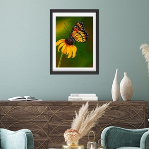 Gouache painting titled 'Flutterby' features a yellow monarch butterfly on a cone flower against a green background. Adds natural elegance to any space.