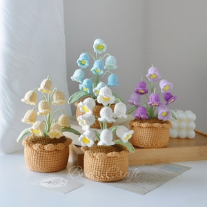 May include: Four crocheted lily of the valley flower arrangements in brown pots. The flowers are white, light blue, yellow, and purple.