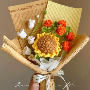 Puede incluir: Un ramo de flores de ganchillo con un gran girasol amarillo, varias flores blancas peque&ntilde;as en forma de campana y flores naranjas similares a rosas con hojas verdes. El arreglo est&aacute; envuelto en papel marr&oacute;n y una hoja con texto impreso.