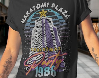 May include: A black t-shirt with a pixelated design of a skyscraper with a star on top. The design says "Nakatomi Plaza Christmas Party 1988".