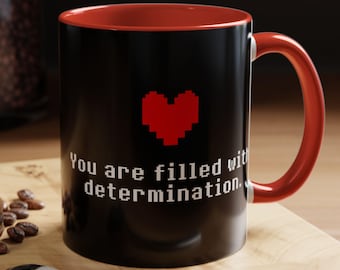May include: Black coffee mug with a red interior and a white pixelated heart with the text "You are filled with determination."