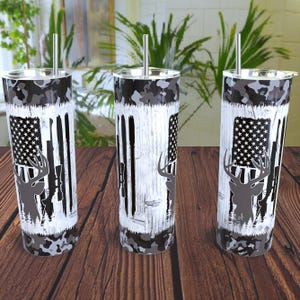 May include: Three stainless steel tumblers with a camouflage pattern, a distressed wood background, and a deer silhouette with an American flag and rifle.