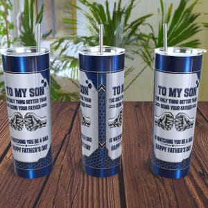 Peut inclure: Un gobelet cylindrique en acier inoxydable avec une finition bleu métallique, un couvercle transparent et une paille en métal. Le design présente un panneau blanc avec un graphique de poings qui se cognent et le texte : TO MY SON THE ONLY THING BETTER THAN BEING YOUR FATHER IS WATCHING YOU BE A DAD HAPPY FATHER'S DAY.