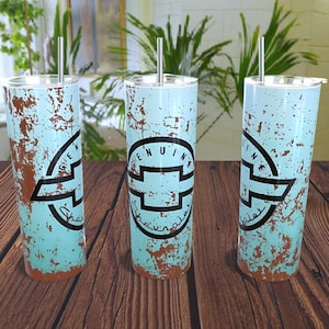 May include: Three stainless steel tumblers with a distressed blue and brown paint design. The tumblers feature a black Chevrolet logo with the text "Genuine Chevrolet" around the logo.