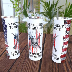 May include: Three white stainless steel tumblers with silver straws. Each tumbler features a design with the American flag, rifles, and a skull. Text on the tumblers reads: "I HAVE THE RIGHT TO BEAR ARMS", "YOUR APPROVAL IS NOT NEEDED".