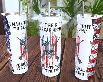 Puede incluir: Tres vasos de acero inoxidable blancos con pajitas plateadas. Cada vaso presenta un diseño con la bandera estadounidense, rifles y una calavera. El texto en los vasos dice: "I HAVE THE RIGHT TO BEAR ARMS", "YOUR APPROVAL IS NOT NEEDED".