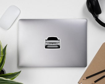 Op de afbeelding: Een witte auto met zwarte koplampen en een zwarte grille. De auto is van voren gericht en staat op een witte achtergrond.