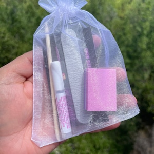 May include: A white organza bag filled with nail care items, including a nail file, a cuticle pusher, a small bottle of glue, and a pink nail buffer.