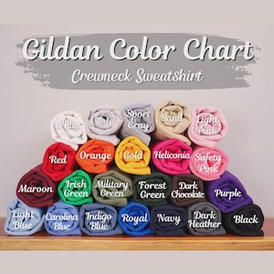 May include: A Gildan Color Chart for crewneck sweatshirts featuring a stacked display of rolled fabric in various colors including white, ash, sport gray, sand, light pink, red, orange, gold, heliconia, safety pink, maroon, green, and black.