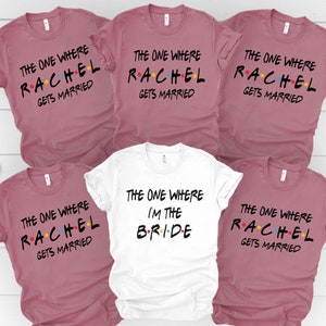 May include: A selection of mauve and white t-shirts. The mauve shirts display the text "The One Where Rachel Gets Married" in black with colourful accents. The white shirt reads "The One Where I'm The Bride".
