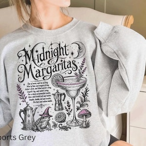 May include: A sports grey crewneck sweatshirt featuring a black and purple graphic print with the text Midnight Margaritas. The design includes a margarita glass, a frog wearing a witch hat, a crescent moon, a coffee pot, and a mushroom.
