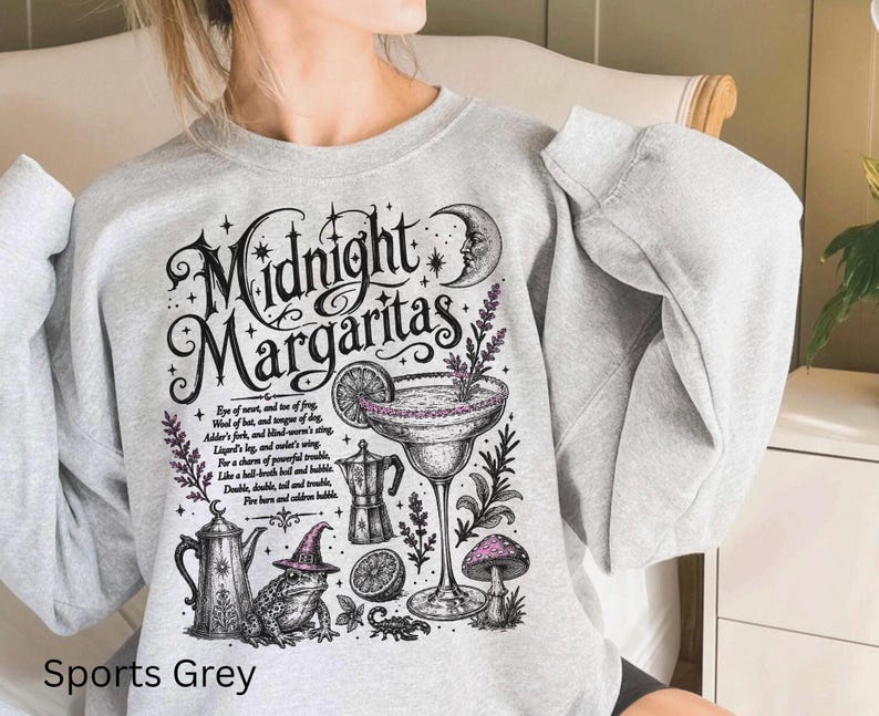 May include: A sports grey crewneck sweatshirt featuring a black and purple graphic print with the text Midnight Margaritas. The design includes a margarita glass, a frog wearing a witch hat, a crescent moon, a coffee pot, and a mushroom.