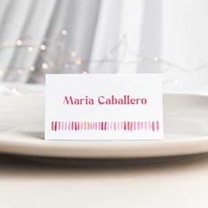 May include: A white place card with pink watercolor stripes at the bottom and the name "Maria Caballero" printed in red.