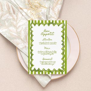 May include: A menu card with the words "Bon Appetit" in green script, featuring a green scalloped border and vertical stripes. The menu lists a starter, main course, and dessert on a pink plate with a floral napkin.