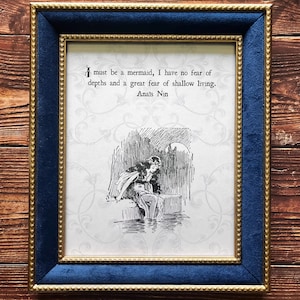 May include: Framed print featuring a quote by Anaïs Nin and a monochrome illustration of a person by water. The frame has a navy blue velvet border and a gold inner edge. The background is cream with a floral design.