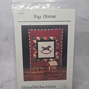 May include: A quilting pattern for a toy horse, featuring a red, white, and green patchwork design. The pattern is titled "Toy Horse" and is from Thimbleberries, located in Hutchinson, Minnesota.