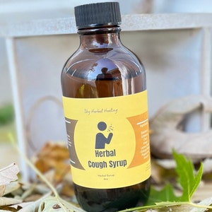 Könnte beinhalten: Eine braune Glasflasche mit schwarzem Deckel und einem gelben Etikett mit der Aufschrift "Sky Herbal Healing" und "Herbal Cough Syrup". Die Flasche steht auf einer Holzoberfläche mit Herbstblättern.