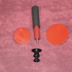 May include: An assortment of auto body repair tools, including two red circular pads, a black handle with a gray foam grip, a black base, and a red handle. The tools are designed for dent removal and repair.