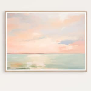 Puede incluir: Pintura de paisaje enmarcada que representa un paisaje marino. La obra de arte muestra un cielo pastel con tonos rosados, melocotón y azul, reflejados en el agua turquesa en calma. La pintura está encerrada en un marco de madera de color claro.