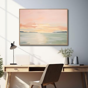 May include: A framed landscape painting depicts a serene sunset over water. The artwork features soft pastel colors of pink, orange, and green, with a wooden frame. The painting hangs above a wooden desk with a black lamp and a wooden chair.