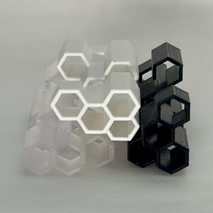 May include: A set of two honeycomb-shaped organizers, one white and one black. The organizers are made of plastic and have a geometric design.
