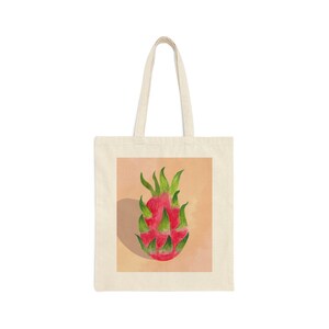 Puede incluir: Una bolsa de tela blanca con una ilustración de fruta de dragón rosa en la parte delantera. La fruta está rodeada de un fondo naranja claro.