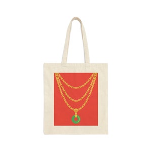 Puede incluir: Una bolsa de tela blanca con un fondo rojo y un collar de cadena dorada con un colgante de jade verde.